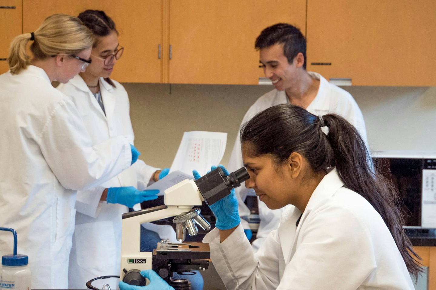 Four researchers in lab coats collaborating inside a modern laboratory.
